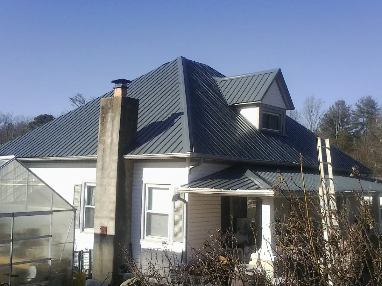 Dark blue standing seam metal roof on a white farmhouse with dormer — Slate & Tile Roof Repair by Roofing Brothers in Rushmore