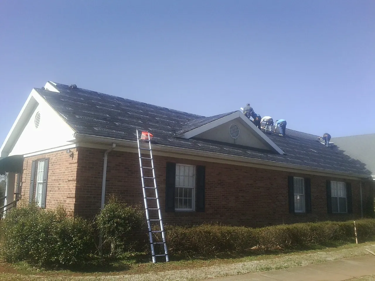 Crew tearing shingles off a brick ranch roof with a ladder set — Metal Roof Repair work by our crew in Rushmore