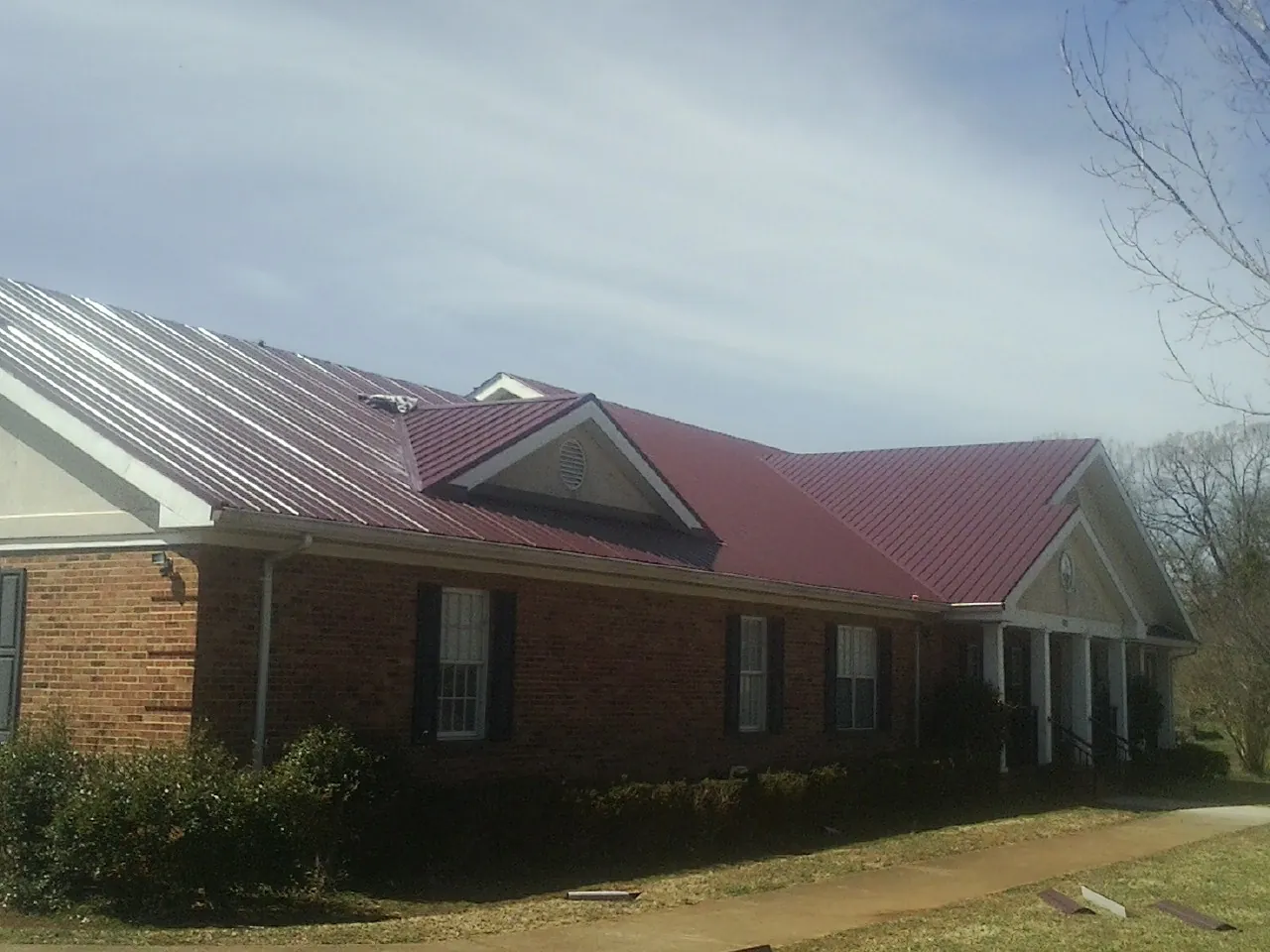 Red metal roof with gabled entries on a long brick building, from a Hail Damage Roof Repair job in Rushmore