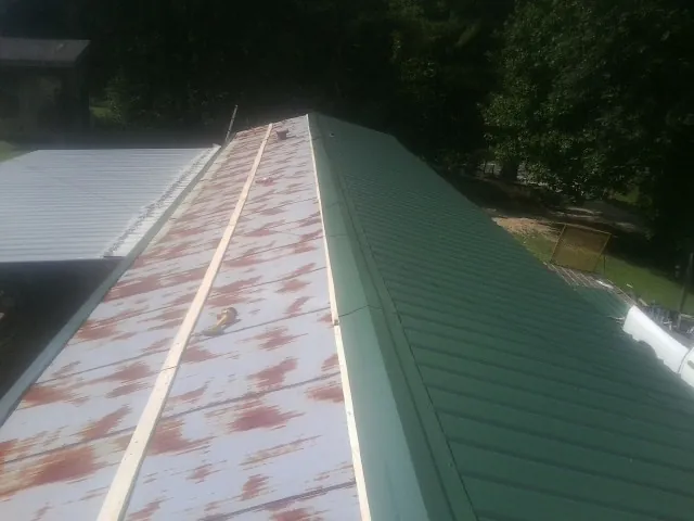 Old rusted panels beside newly installed green metal roofing — Wind Damage Roof Repair by Roofing Brothers in Rushmore