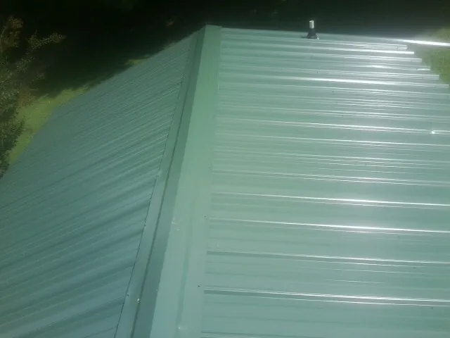 New green metal panels meeting at the ridge of a roof — Flat Roof Repair work by our crew in Rushmore