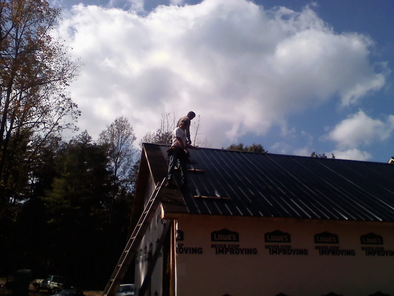 Roofer fastening dark metal panels high against a cloudy sky, from a Roof Inspection job in Rushmore