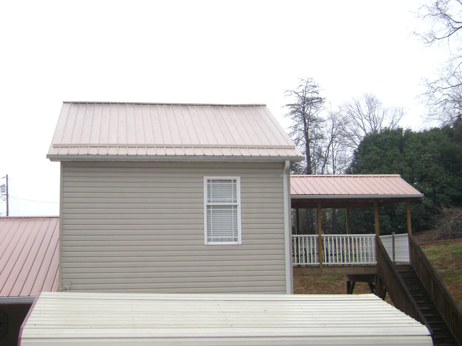 Tan metal roofs on a two story addition and attached porch, from a Roof Replacement job in Rushmore